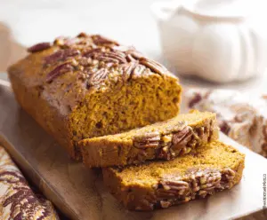 Golden Pumpkin Pecan Bread loaf topped with toasted pecans and a sprinkle of cinnamon, perfect for fall baking.