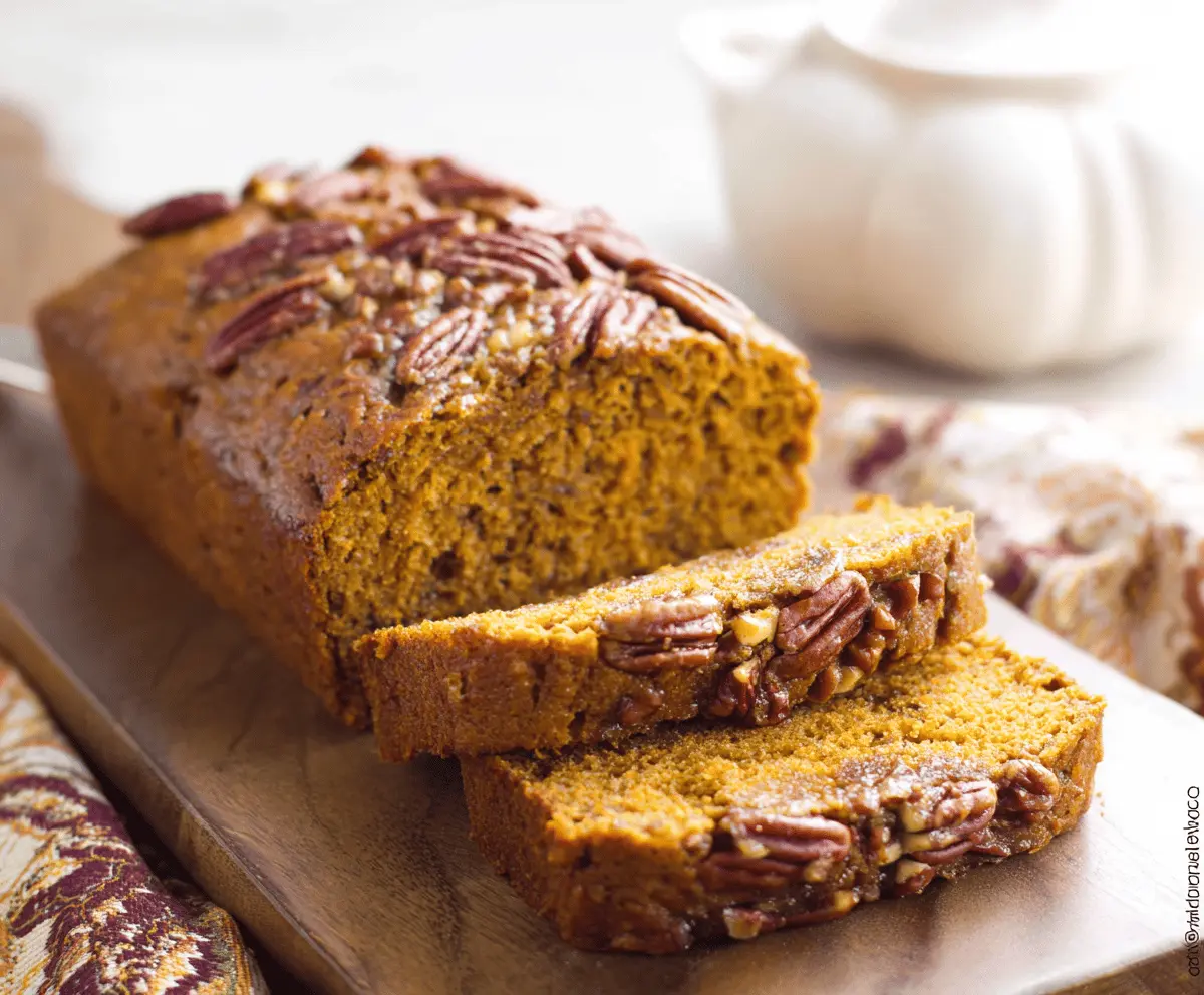Golden Pumpkin Pecan Bread loaf topped with toasted pecans and a sprinkle of cinnamon, perfect for fall baking.
