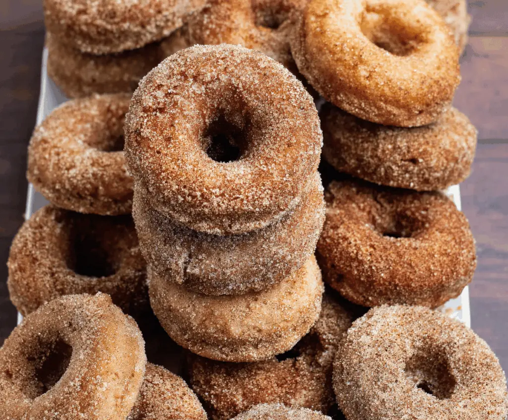 Freshly baked apple cider donuts on a rustic wooden plate, topped with cinnamon sugar, perfect for fall indulgence.