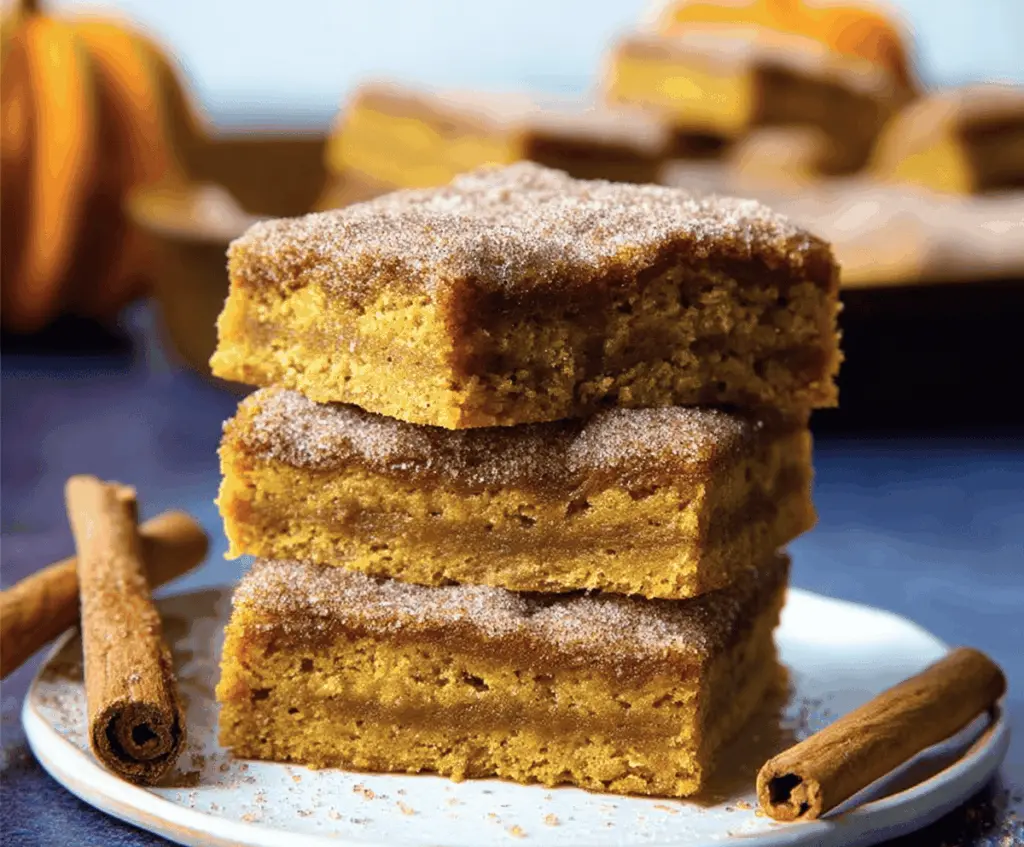 Delicious Pumpkin Snickerdoodle Bars topped with cinnamon sugar and cream cheese frosting on a rustic wooden table