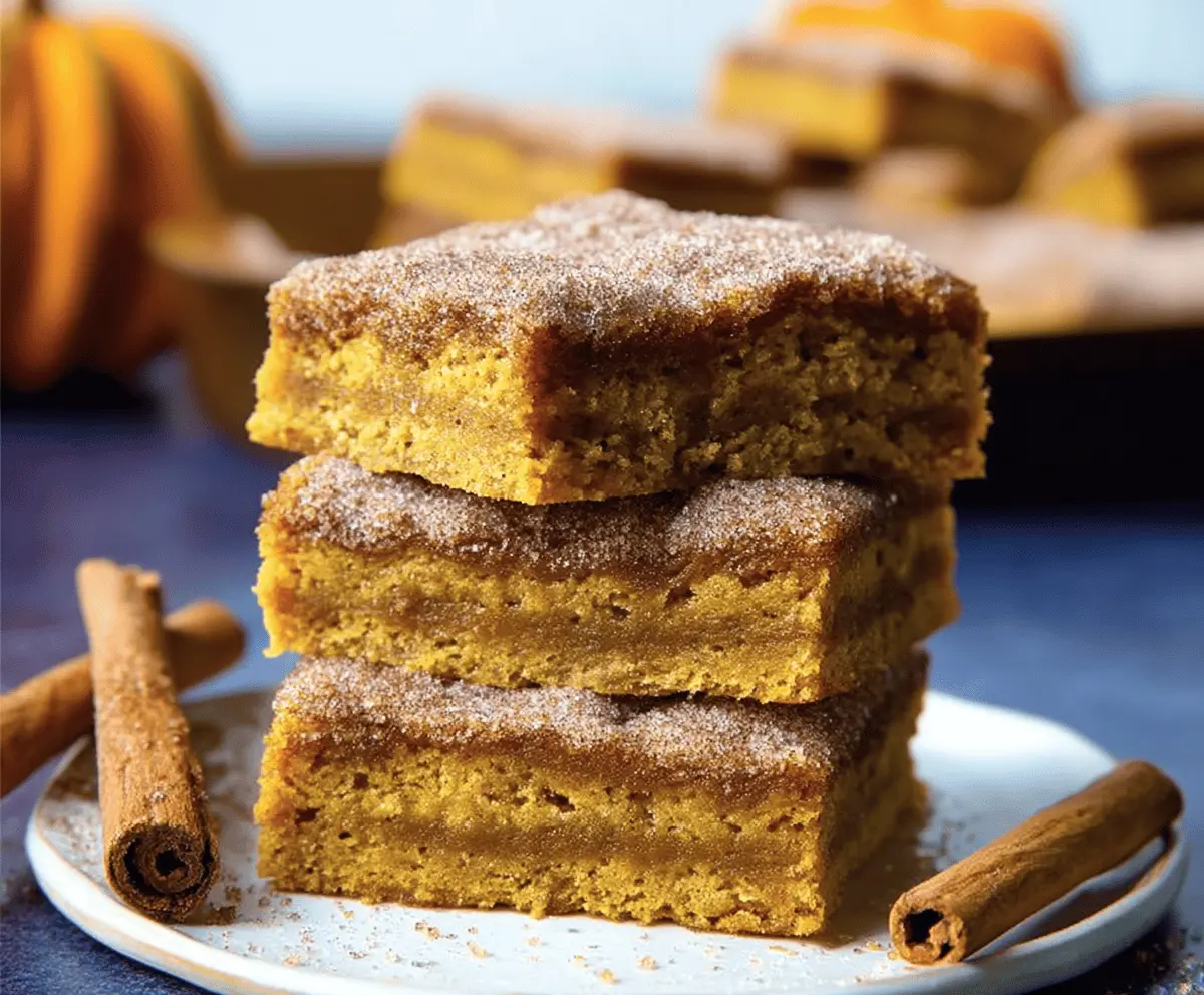 Delicious Pumpkin Snickerdoodle Bars topped with cinnamon sugar and cream cheese frosting on a rustic wooden table