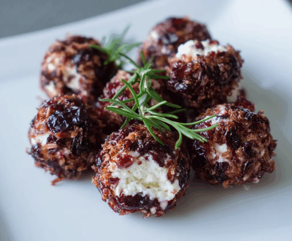 Cranberry Goat Cheese Balls on a platter with fresh cranberries and herbs, perfect appetizer for holidays.
