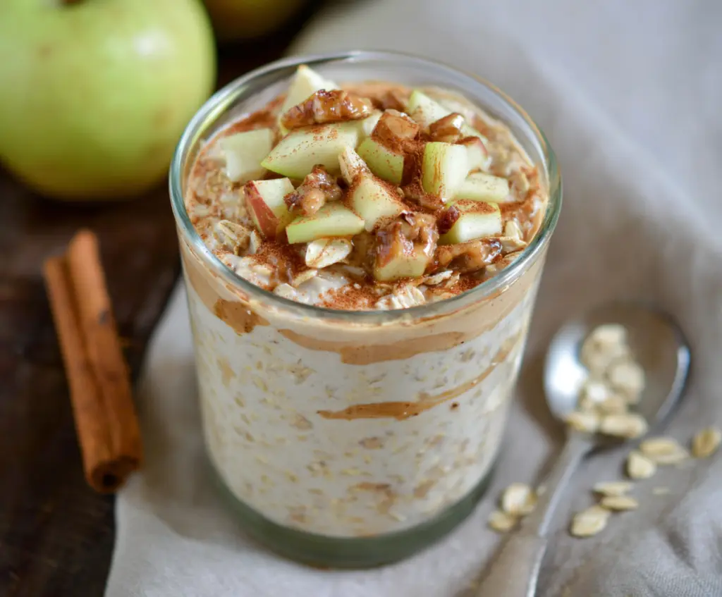 Creamy apple cinnamon protein overnight oats in a glass jar topped with fresh apple slices and cinnamon for a healthy breakfast.