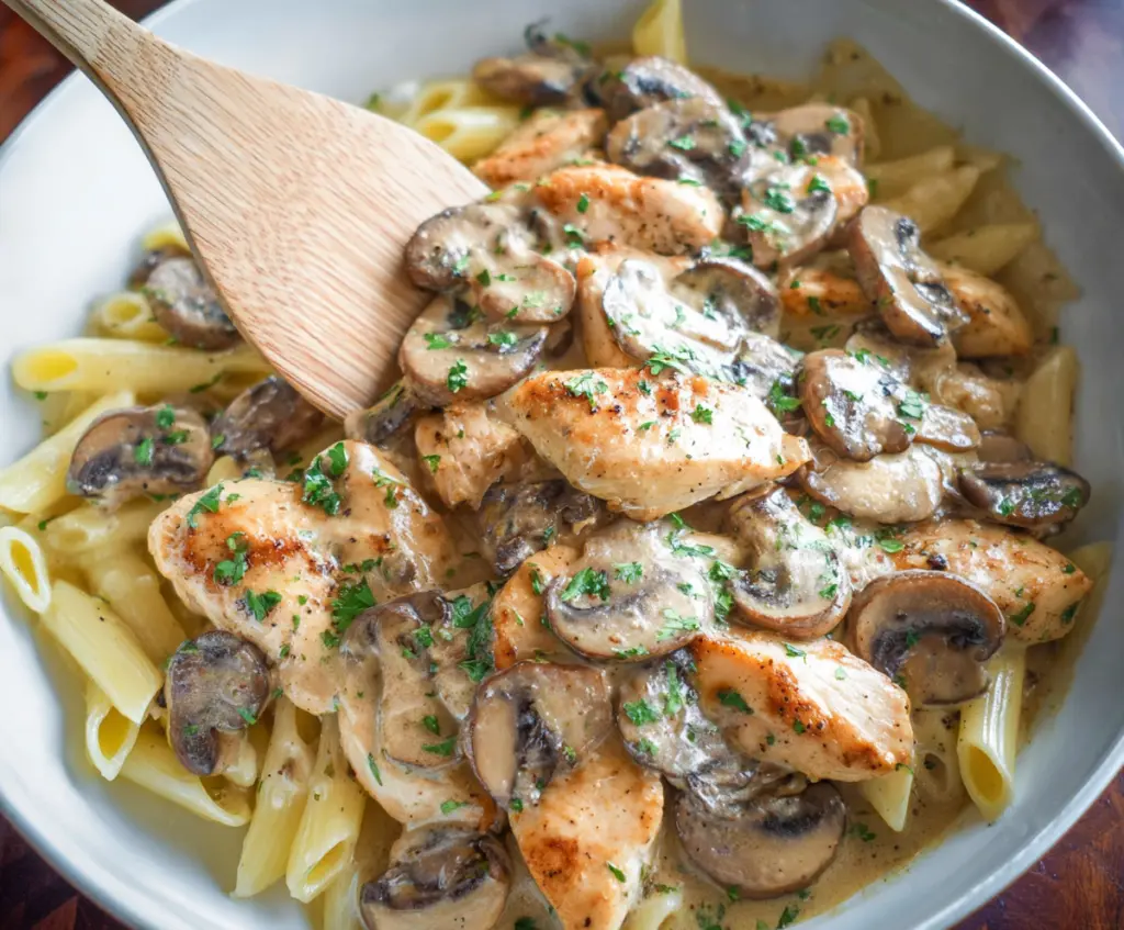 Delicious chicken mushroom pasta served on a white plate with fresh herbs.