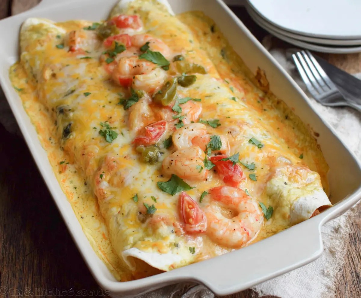 Delicious creamy shrimp enchiladas garnished with fresh herbs on a white plate.