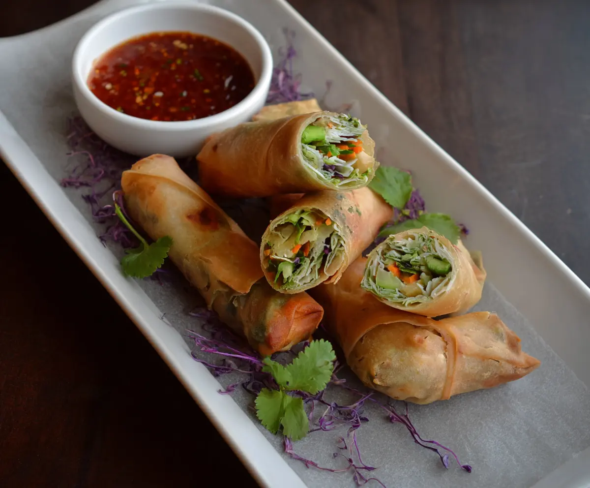 Crispy chicken vegetable spring rolls with fresh dipping sauce on a white plate.