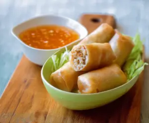 Fresh Thai chicken spring rolls wrapped in rice paper served with sweet chili dipping sauce, ideal for appetizers and snacks.